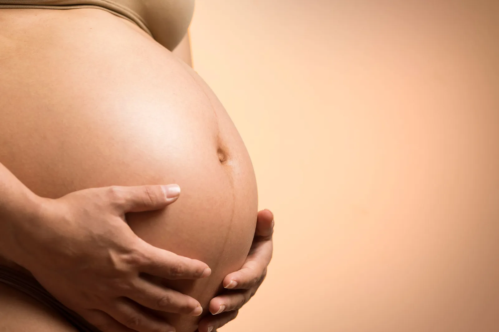 Mãos de uma gestante segurando a barriga